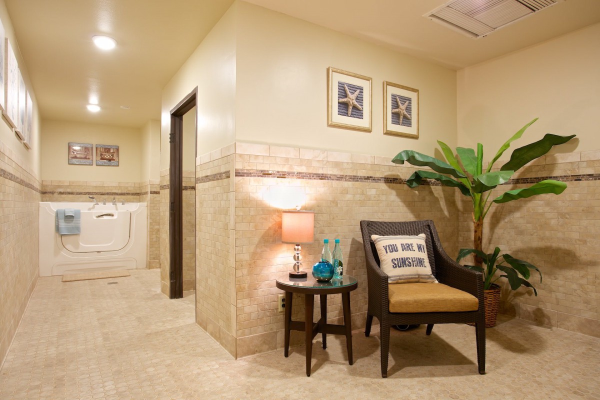 A well-decorated lobby area featuring a chair, a side table with a lamp and decorative items, and framed artwork on the wall.