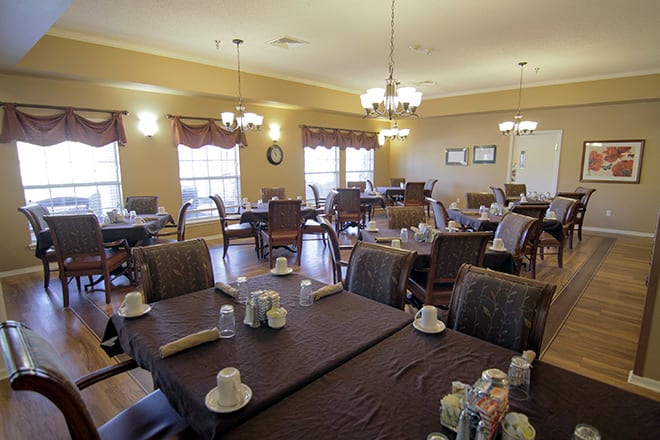 A spacious dining room with neatly arranged tables and chairs, illuminated by elegant chandeliers.