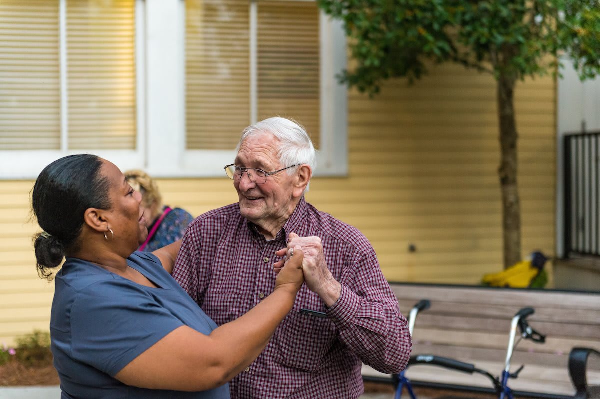 An elderly couple joyfully dancing together outside.