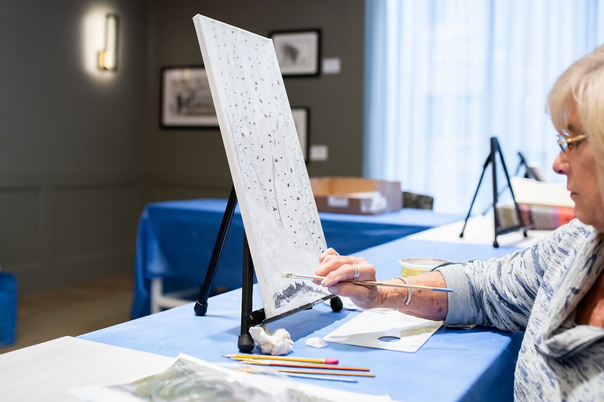 A person working on a paint-by-numbers canvas at a table.