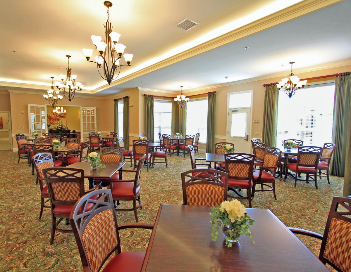 A spacious dining room with elegant decor, featuring multiple tables and chairs under ornate chandeliers.