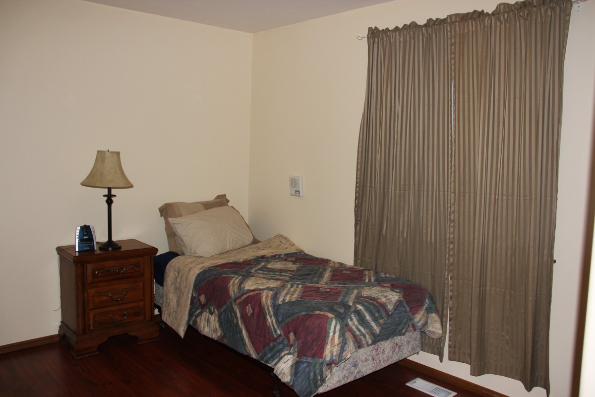A cozy bedroom with a single bed, nightstand, and lamp next to a window with curtains.