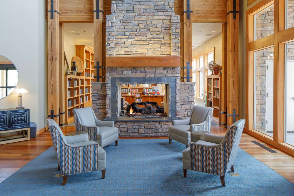 A cozy library room with a central stone fireplace surrounded by chairs and bookshelves.