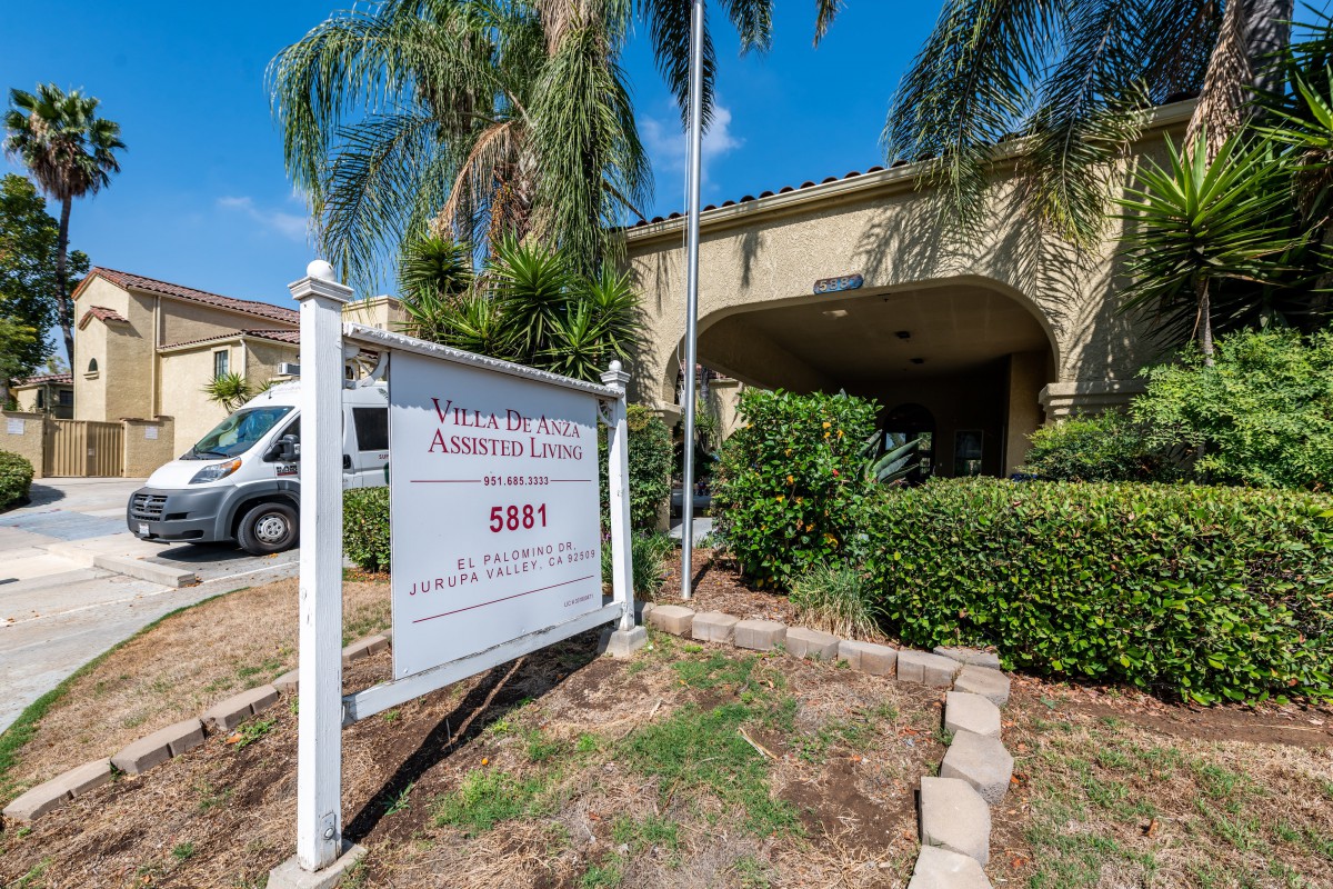 A building entrance with a sign and palm trees in the foreground.