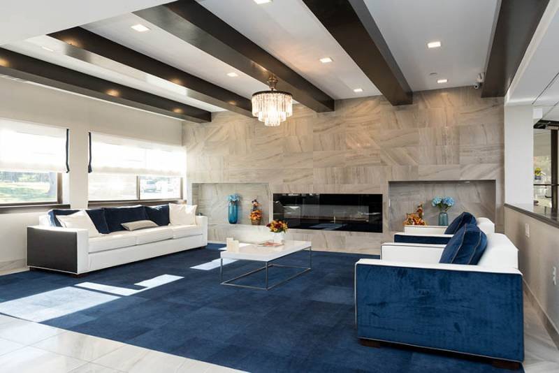 A modern living room with a blue carpet, stylish furniture, beamed ceiling, and a large fireplace.