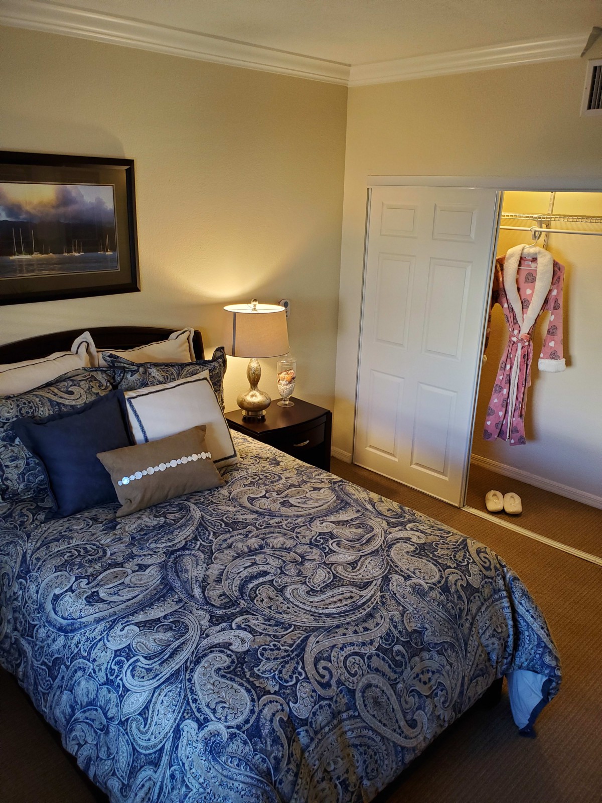 A cozy bedroom with a neatly made bed, bedside lamp, and an open closet displaying a robe.