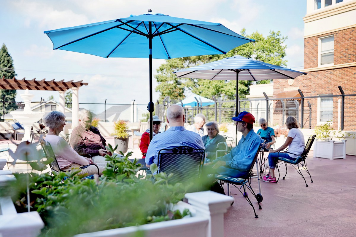 A group of people enjoying a social gathering on a patio under blue umbrellas.