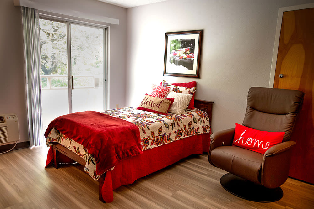 A cozy bedroom with red-themed decor featuring a single bed and a comfortable armchair.