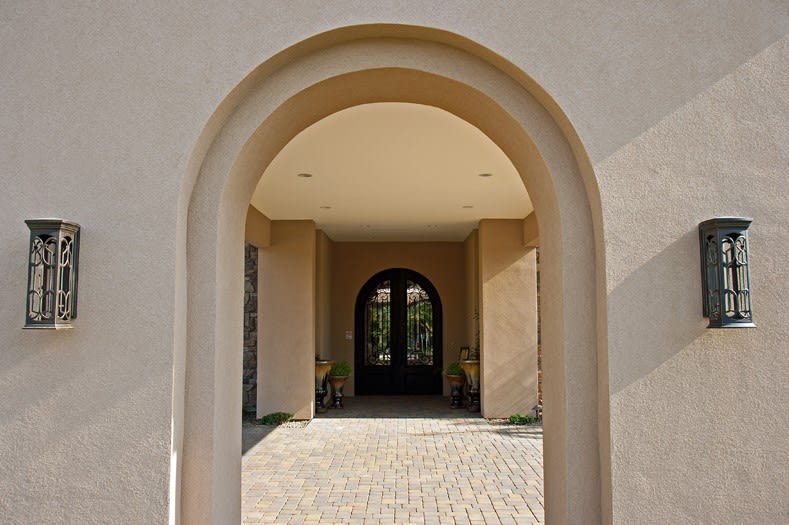 An elegant archway leads to a stylish entrance door of a building.