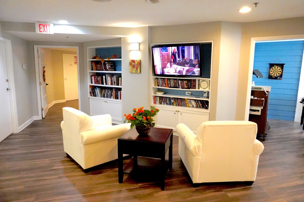 A cozy living room with two white chairs facing a television and built-in bookshelves.