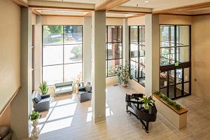 A modern lobby featuring a piano, large windows with plenty of natural light, and indoor plants.