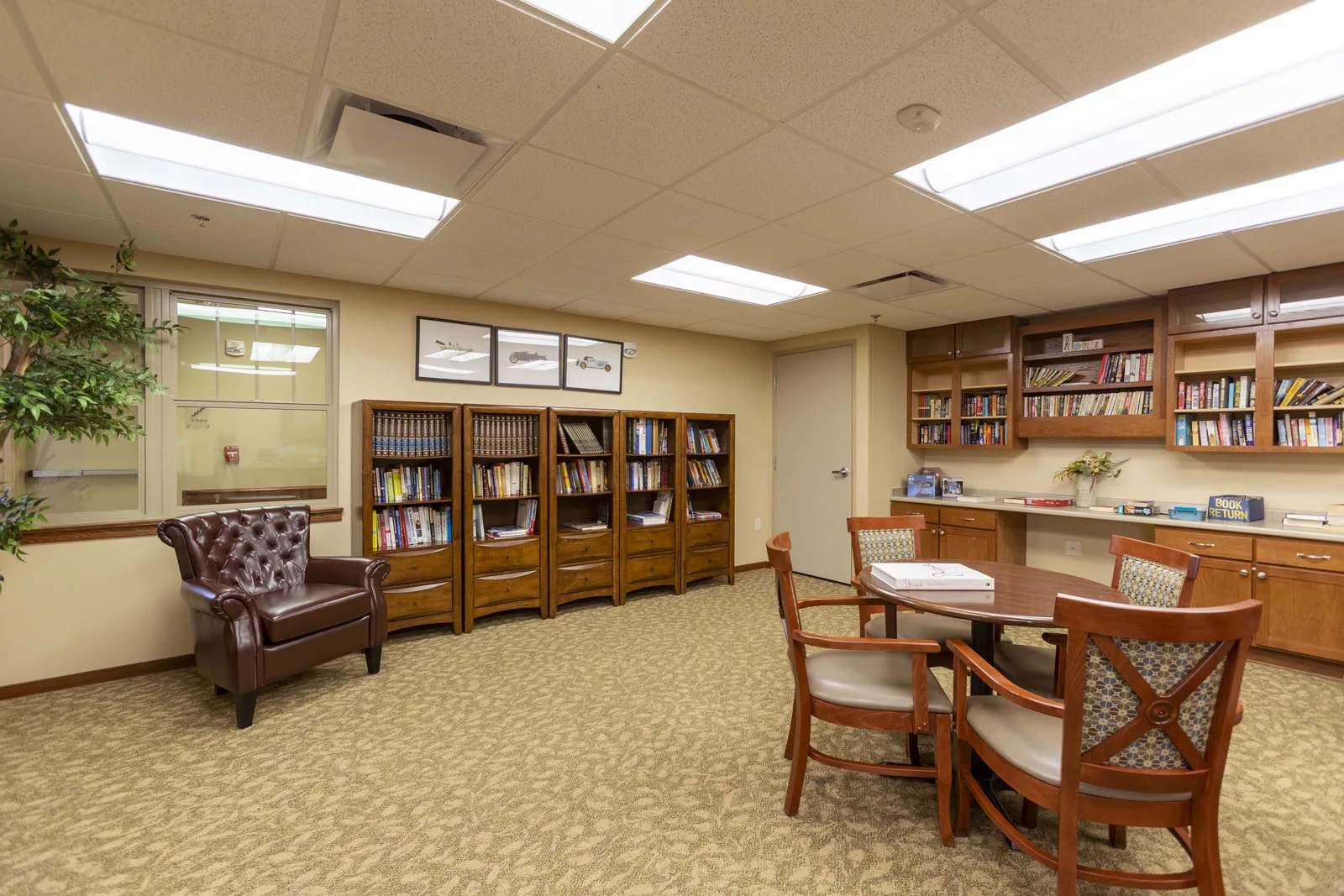 A cozy library space with bookshelves, a meeting table, and comfortable seating.