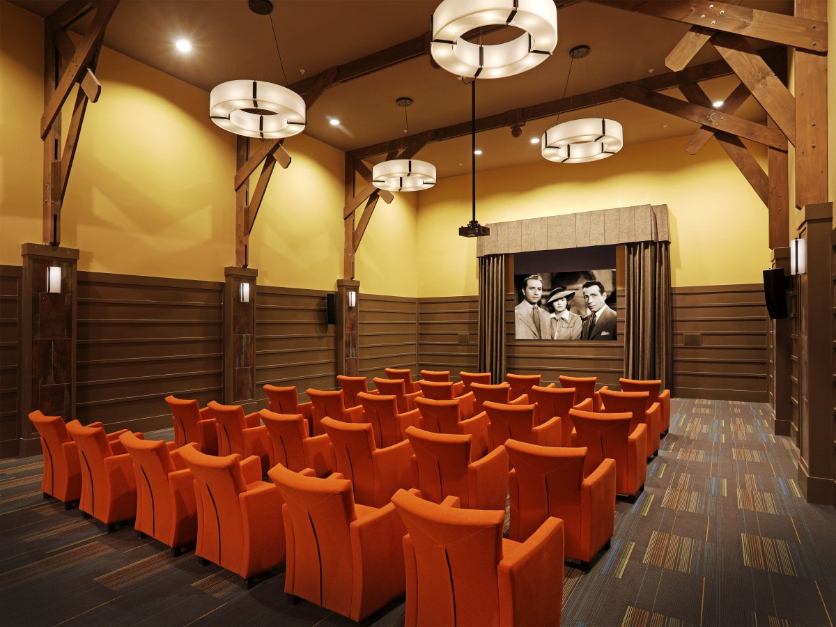 A cozy theater room with orange seating and a classic film on the screen.