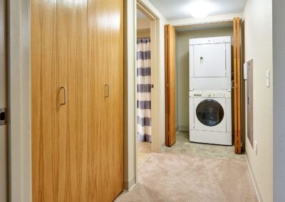 A hallway featuring a stacked washer and dryer unit with wooden closet doors and carpet flooring.