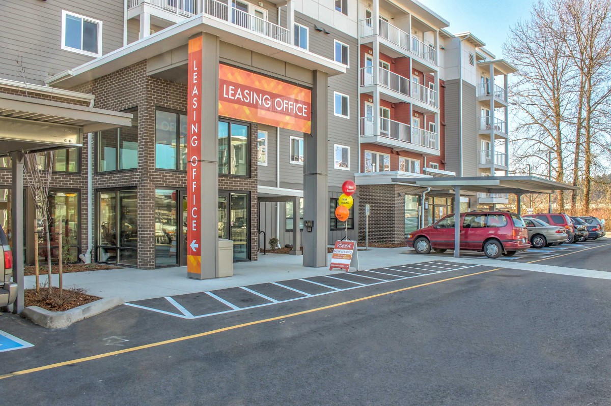 A modern apartment building with a leasing office entrance and adjacent parking lot.
