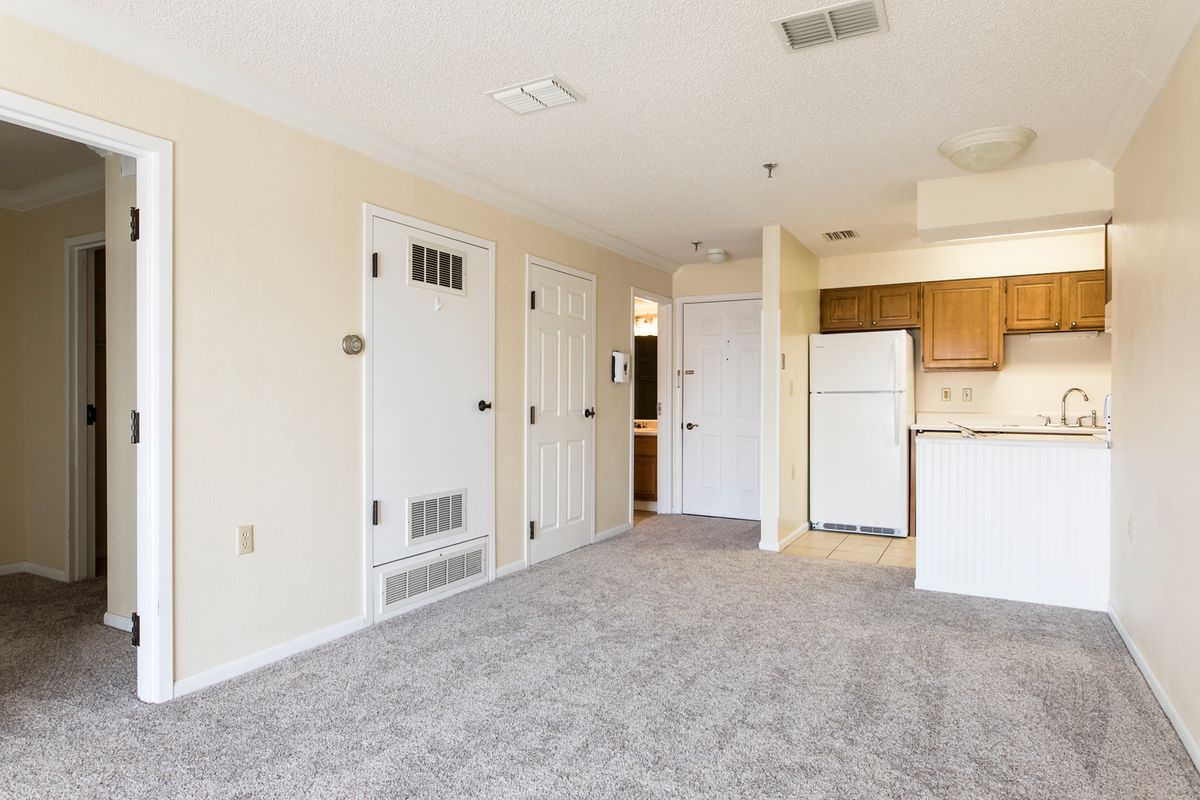 An empty apartment with carpet flooring and an open kitchen area.