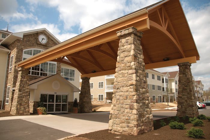 A residential building entrance with stone pillars and a clock under a clear sky.