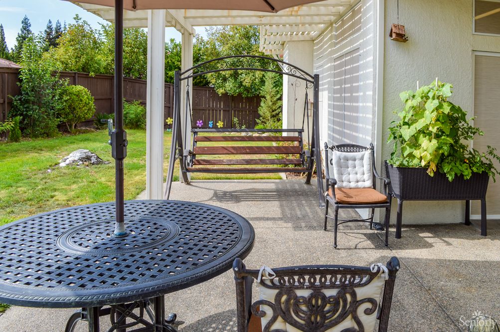 A cozy outdoor patio featuring a swing, iron table, and chairs overlooking a green backyard.