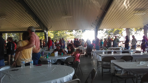 A bustling outdoor gathering with people seated at tables under a covered pavilion.