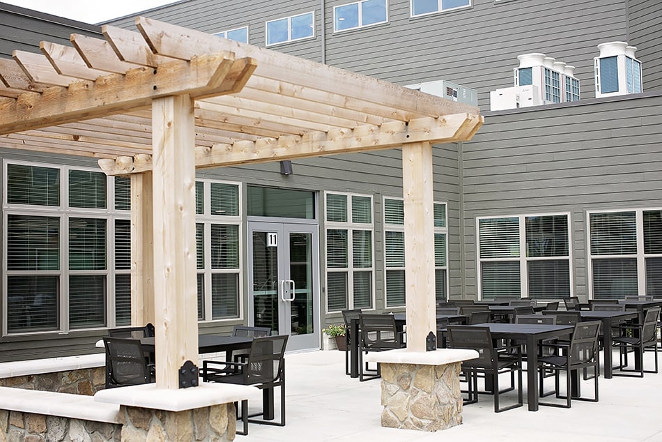 A modern outdoor patio area featuring a wooden pergola, tables, and chairs.