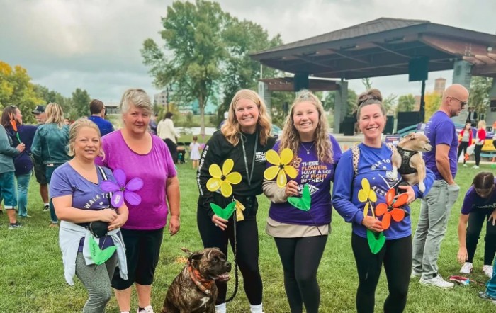 A group of women holding colorful flowers pose together at an outdoor event.