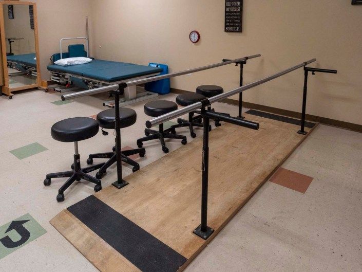 A physical therapy room featuring parallel bars and stools for rehabilitation exercises.