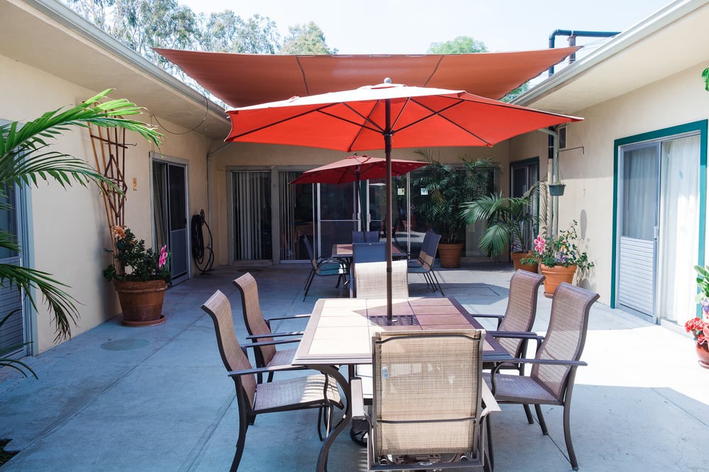 A cozy outdoor patio with a table, chairs, and red umbrellas providing shade.