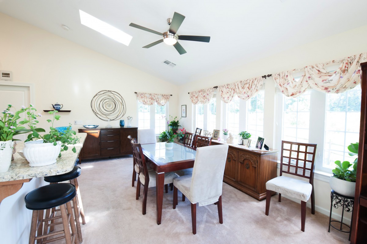 A bright dining room with a large table, chairs, and ample sunlight streaming through the windows.