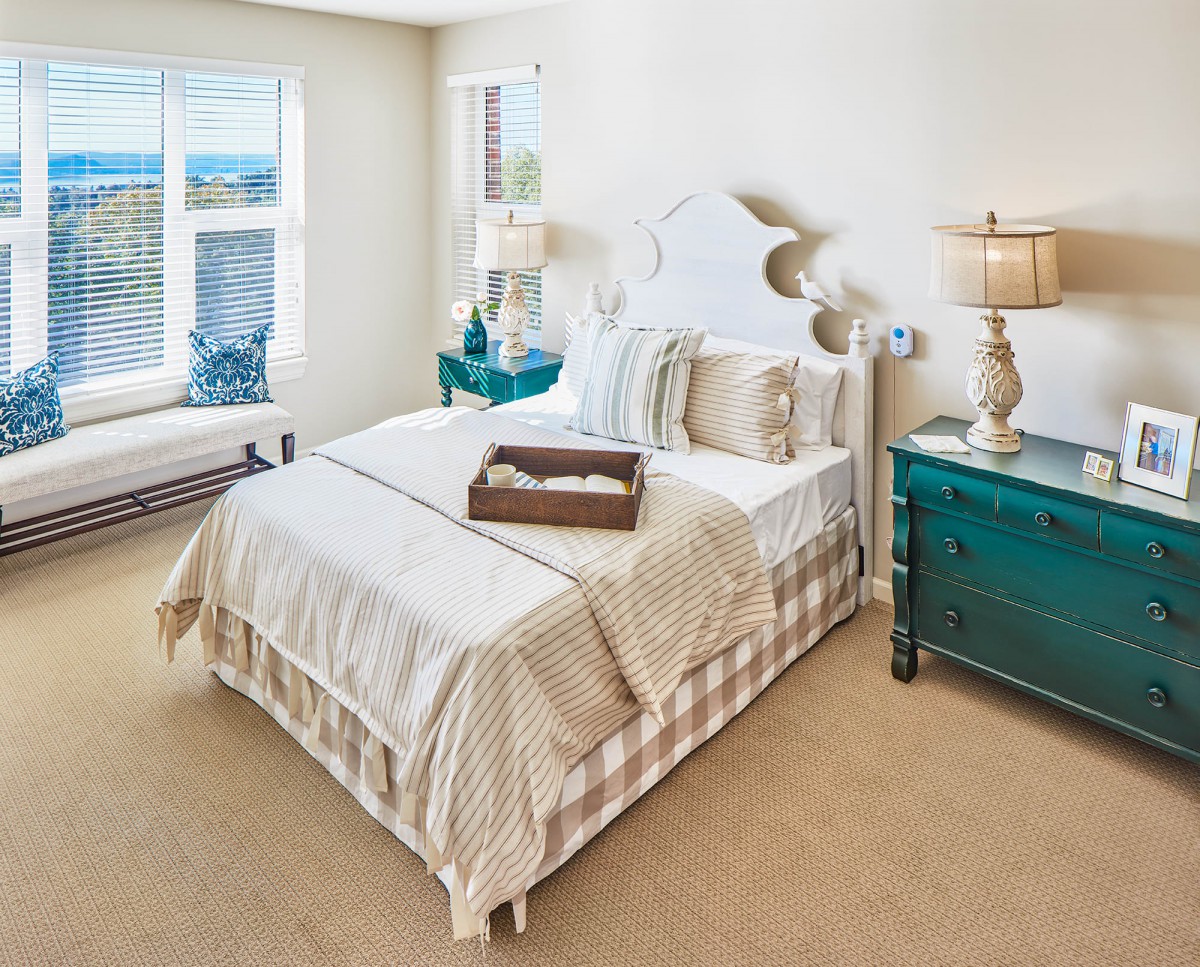 A cozy bedroom interior featuring a neatly made bed, decorative pillows, and two bedside lamps under natural light from a window.