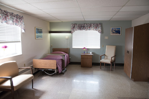 A spacious and well-lit hospital room featuring a bed, chair, and bedside table.