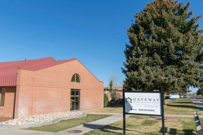 A brick building with a red roof next to a sign and tree on a clear day.