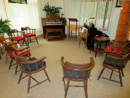 A cozy room arranged with chairs in a circle, featuring a piano and decorative plants.
