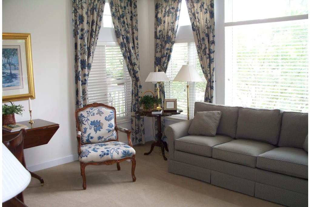 A cozy living room with a gray sofa, floral armchair, and patterned curtains.