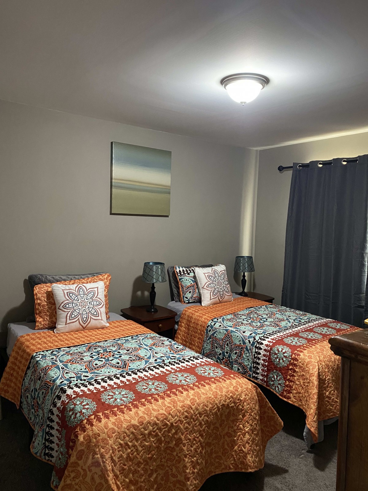 A cozy bedroom featuring twin beds with colorful bedding, complemented by lamps and dark curtains.