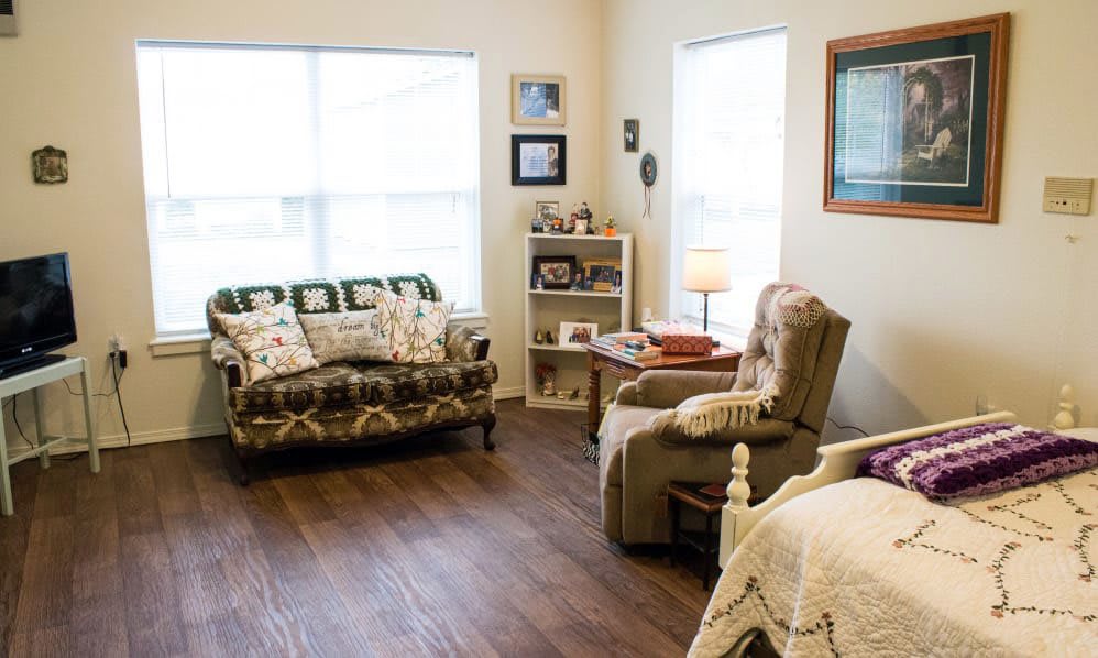 A cozy living room with a sofa, armchair, bookshelf, and table lamp.