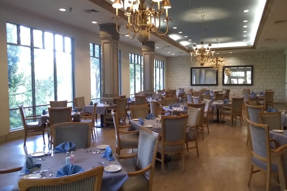 An elegant dining room with neatly arranged tables and chairs, adorned with chandeliers.