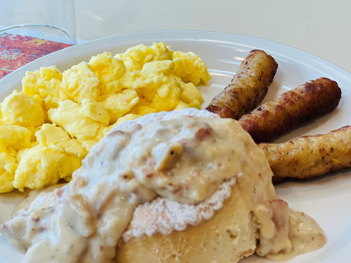 A hearty breakfast plate featuring scrambled eggs, sausage links, and biscuits smothered in gravy.