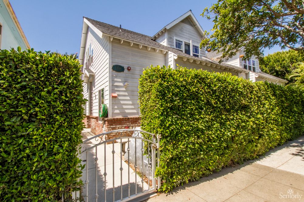 A sunny day view of a residential house with a white exterior and neatly trimmed hedges.