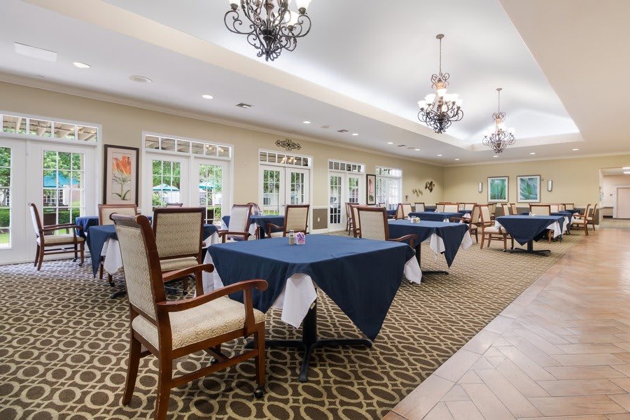 Elegant dining room with neatly arranged tables and chairs, adorned with chandeliers.