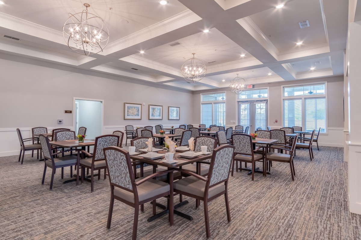 A spacious and elegantly designed dining room featuring multiple tables and chairs, with chandeliers providing ambient lighting.