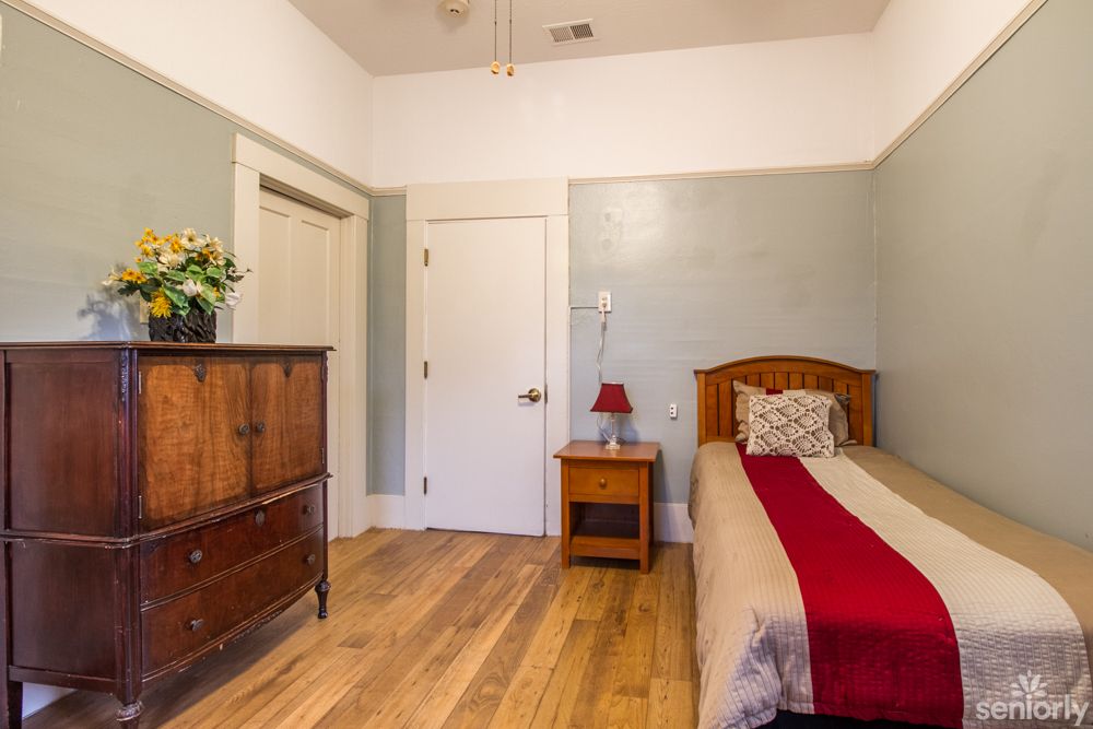 A simple bedroom with a single bed, wooden furniture, and minimal decor.
