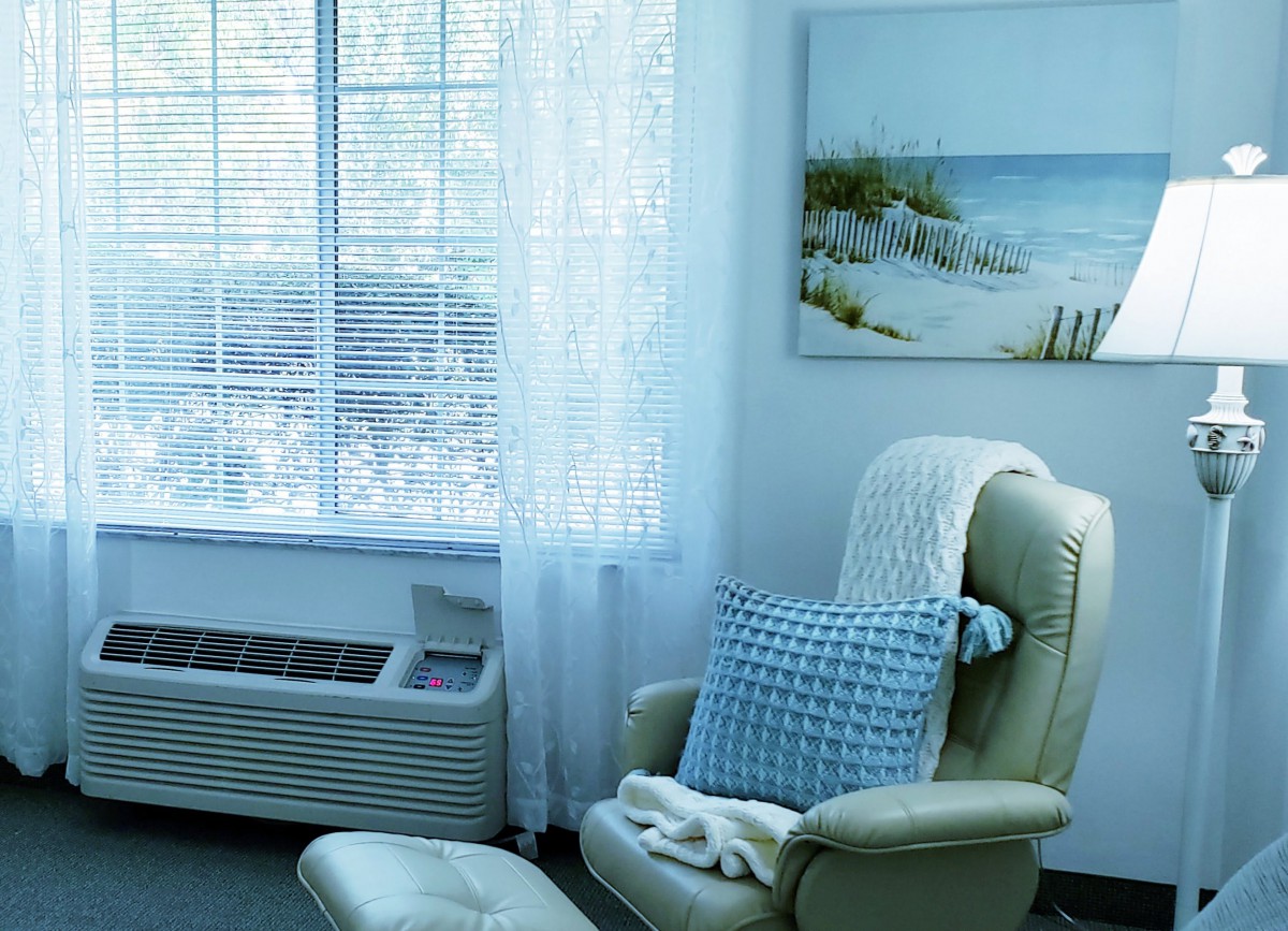 A cozy living room corner with an armchair, pillow, and blanket by a sunlit window.