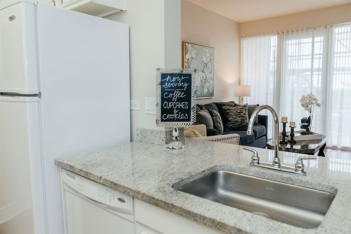A modern kitchen countertop with a sink and a chalkboard sign offering coffee, tea, and cookies.