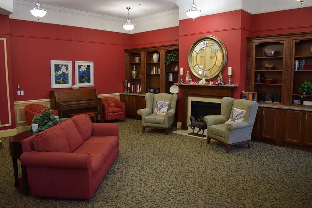 A cozy living room with red walls, featuring a sofa, armchairs, a fireplace, and bookshelves.