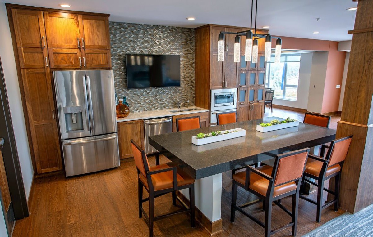 A modern kitchen with wooden cabinets, stainless steel appliances, and a stylish dining area featuring pendant lighting and bar stools.
