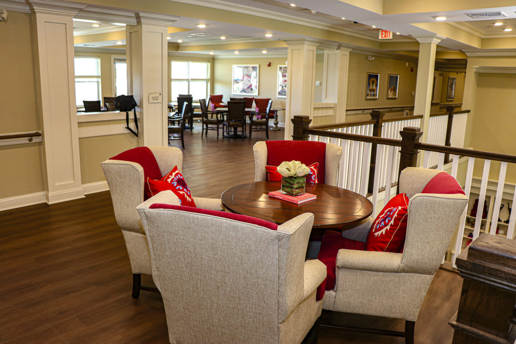 A modern lounge area featuring a round table surrounded by armchairs with decorative red pillows.