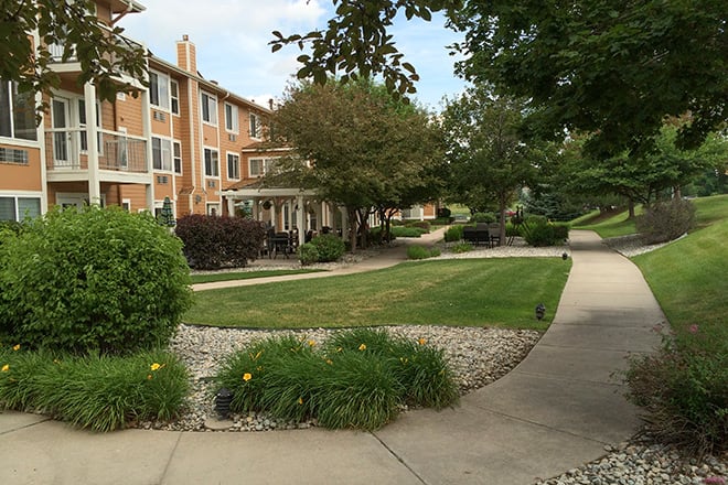 A well-maintained residential area with a sidewalk, greenery, and surrounding trees.