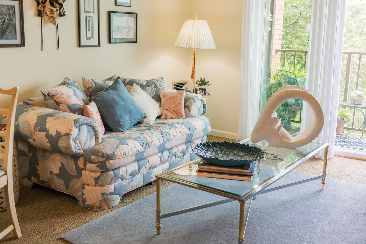A cozy living room with a floral sofa, decorative pillows, and a glass coffee table.