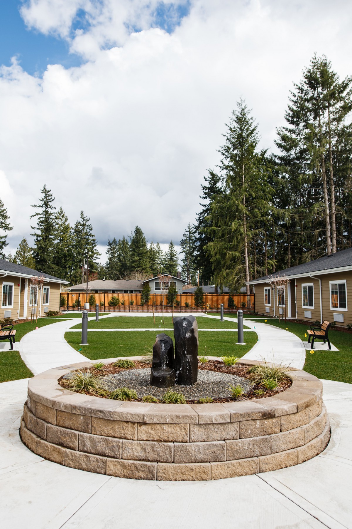A serene courtyard with a central fountain, surrounded by pathways, benches, and lush greenery.