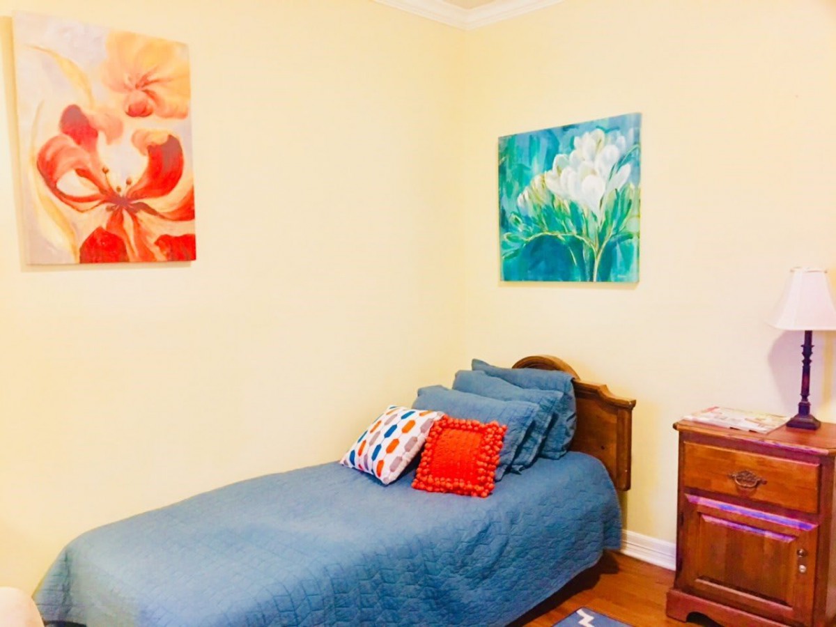 A cozy bedroom with a single bed, colorful artworks on the walls, and vibrant pillows.